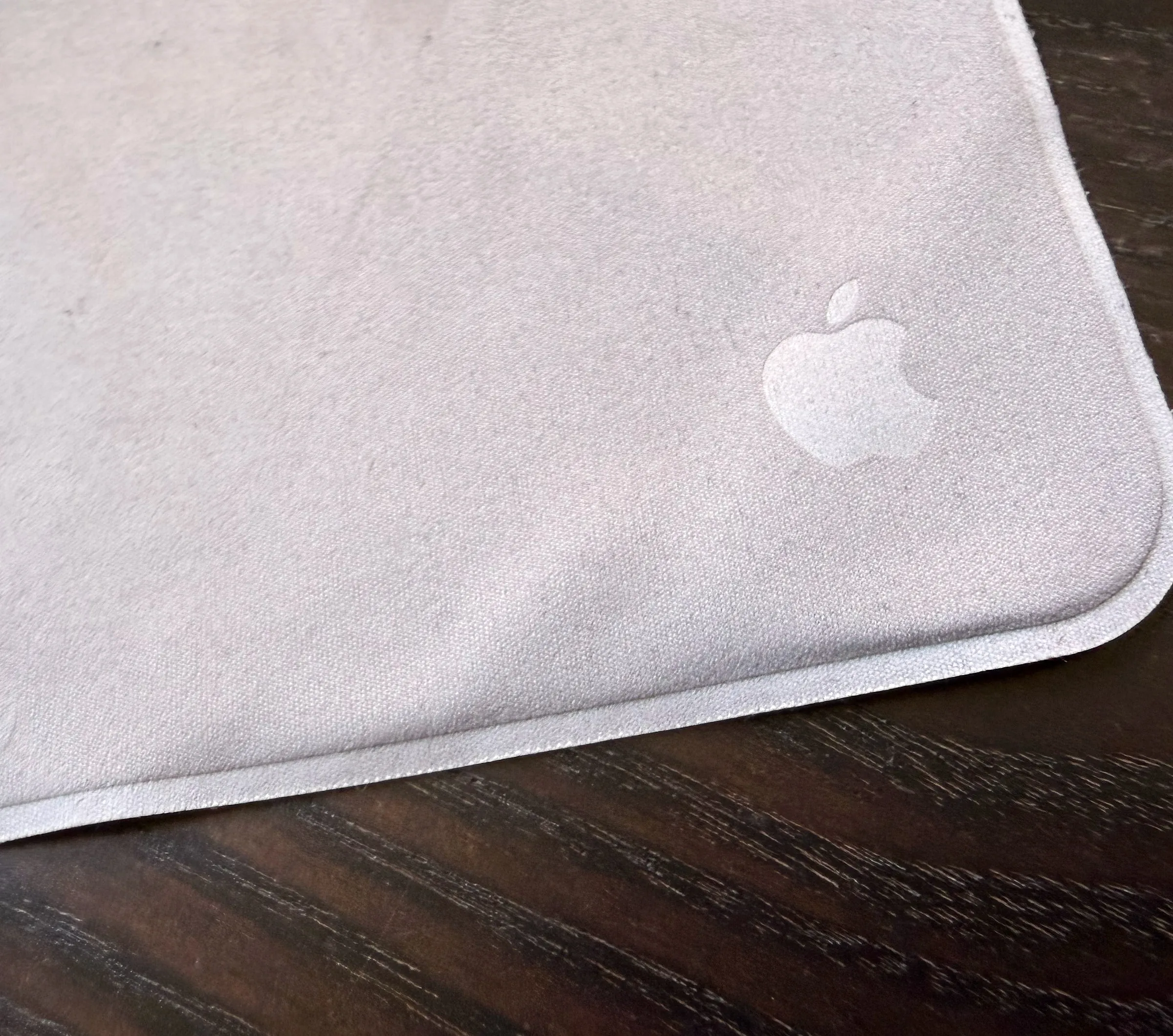 One corner of the cloth turned up on a dark wood desk, the grey Apple logo woven into the weave