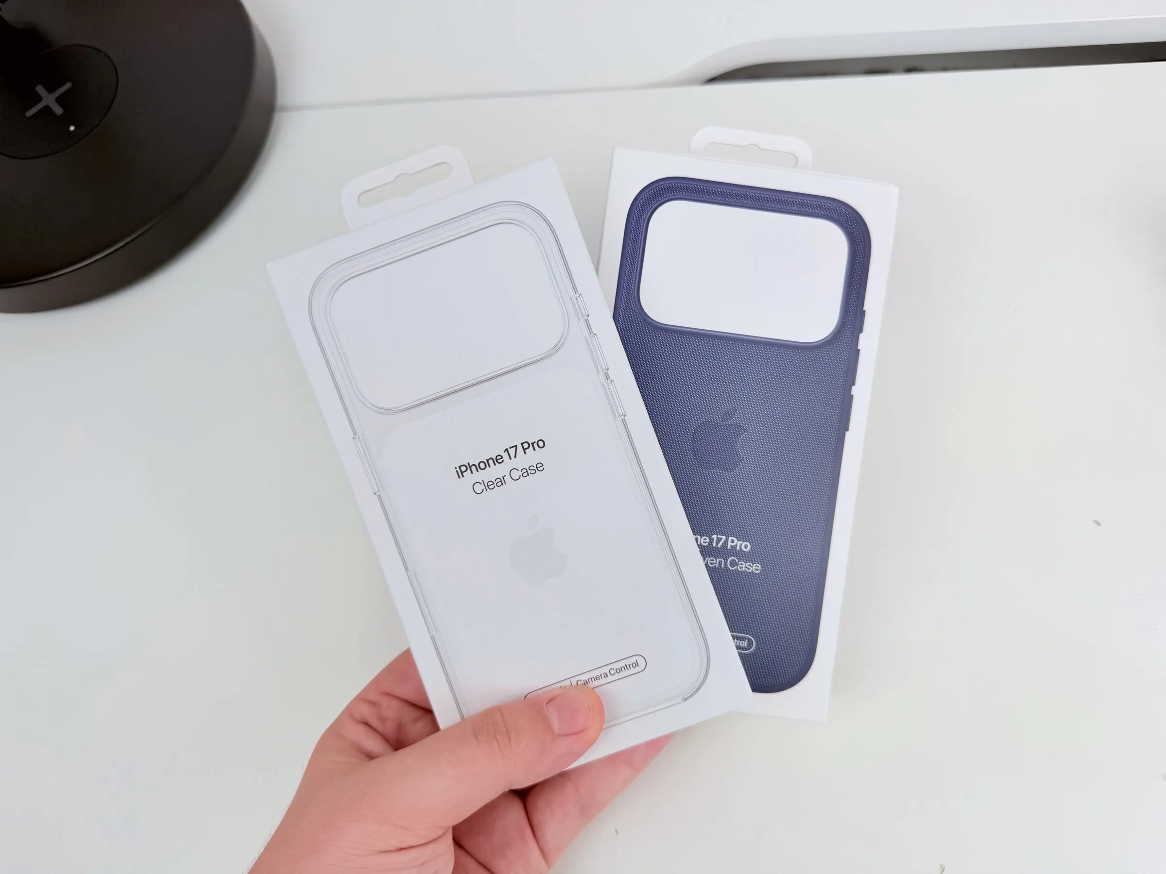 Le confezioni delle due custodie viste dall'alto e tenute in mano: la Clear Case trasparente davanti, la TechWoven blu notte dietro